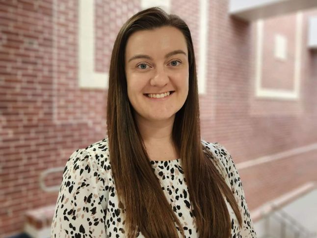  Picture of Ms. Moran standing in front of a brick wall